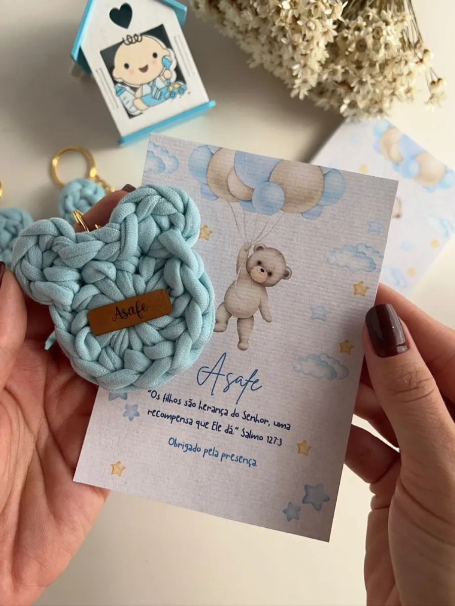Chaveiro de coração em fio de malha azul claro com etiqueta de couro personalizada, ao lado do cartão de lembrança