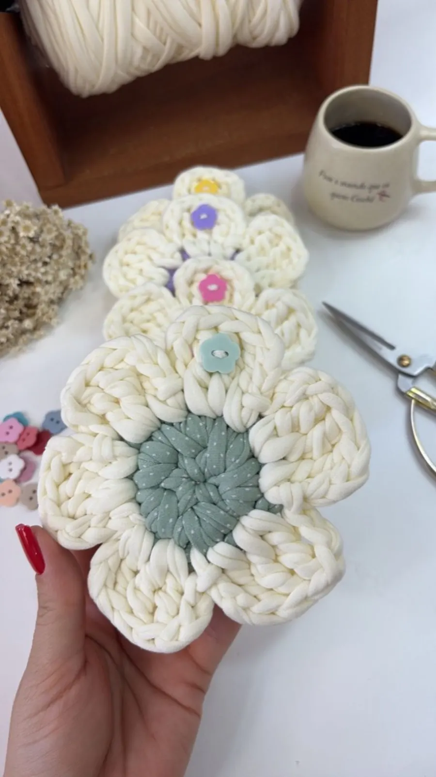 Porta-copo em formato de flor em fio de malha cru com miolo verde-sálvia e botões coloridos